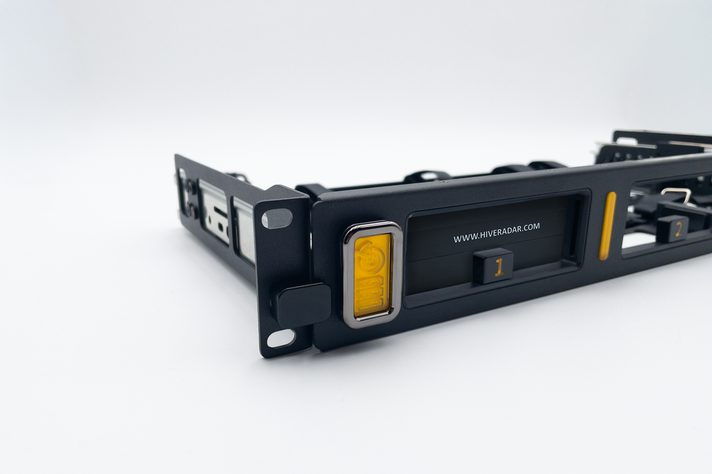 A close-up of a black metal server rack frame with yellow accent LED lights and a slot cover fitted into a unit cradle, photographed on a clean white studio background.